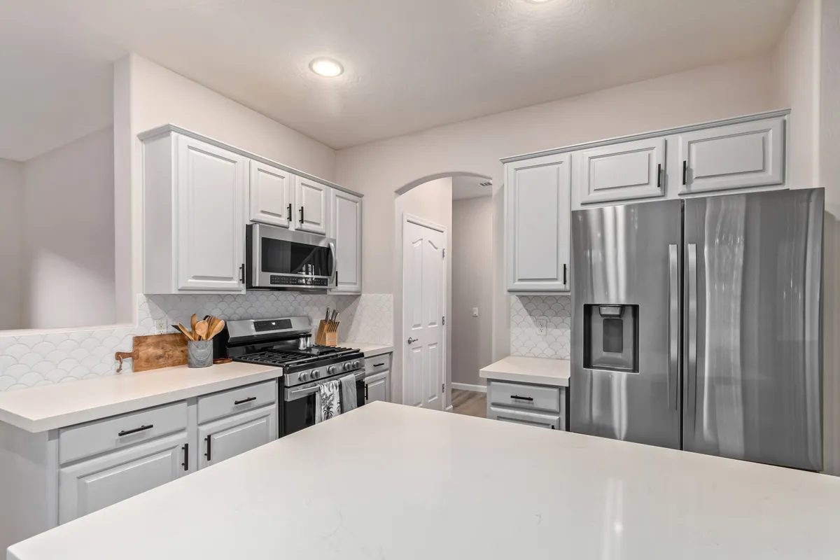 A modern kitchen with a large island, sleek stainless steel appliances, white cabinetry, and a stylish hexagonal backsplash. The setting exudes warmth and is ideal for family gatherings, meal prep, and casual entertaining.