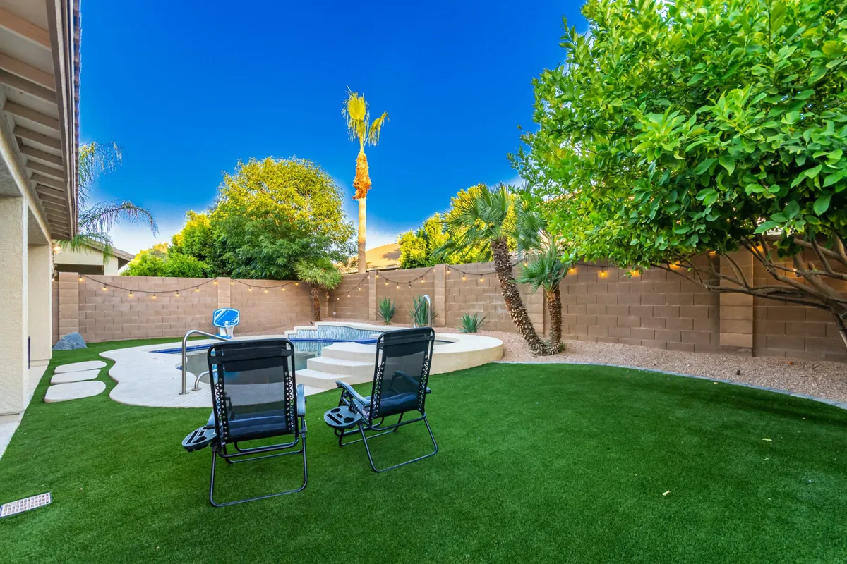 A tranquil corner of the backyard featuring two lounge chairs beside a bubbling hot tub, surrounded by manicured greenery. The area offers a private, peaceful setting ideal for post-game relaxation or enjoying sunset views.