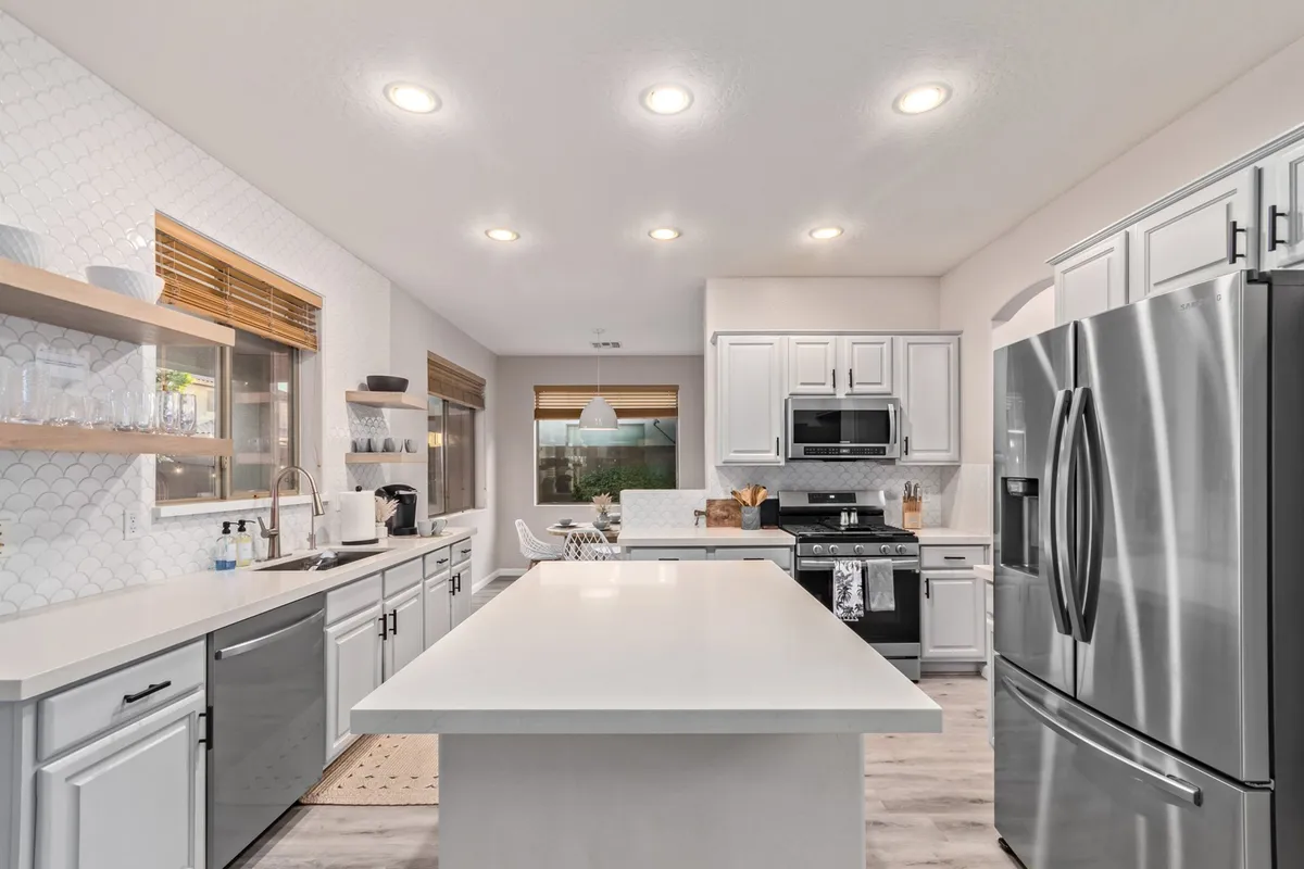 A bright and spacious kitchen featuring a central island, stainless steel appliances, and open shelving. The layout offers ample counter space for preparing meals and is designed to accommodate group gatherings around the island. Warm lighting and modern finishes create an inviting atmosphere.