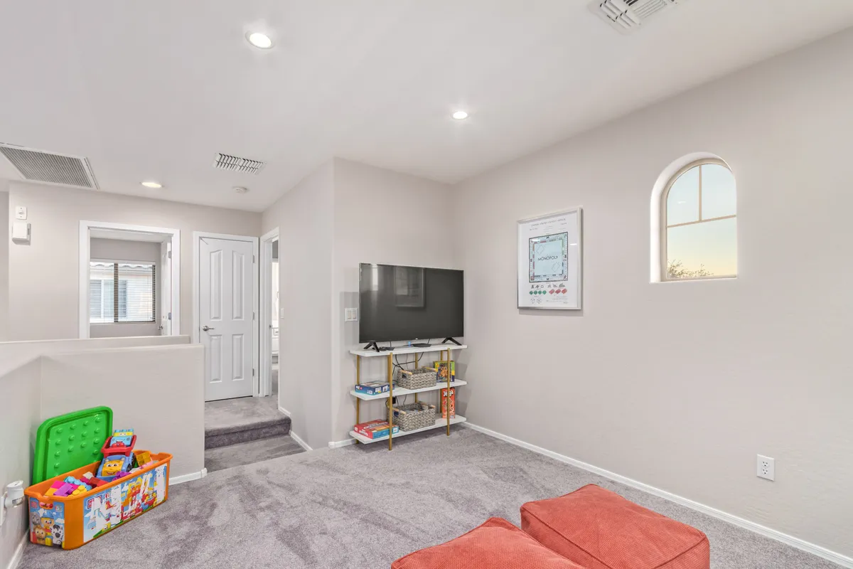 A cozy upstairs loft-style living space featuring a television, a colorful toy bin for families, an inviting orange couch, and framed artwork. The setting is playful yet relaxing, perfect for movie marathons or family game nights.