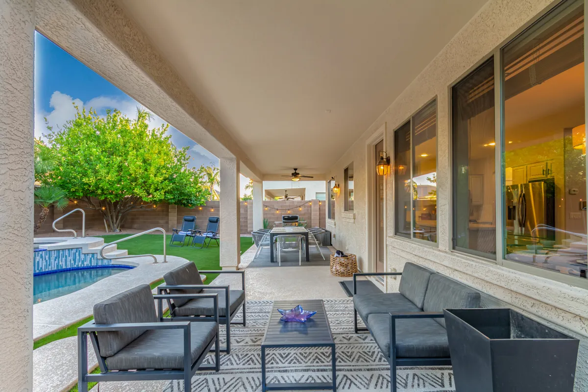 An inviting backyard scene with a spacious patio, swimming pool, lush landscaping, and an outdoor dining area. Ample seating and a fire pit suggest opportunities for both group gatherings and quiet moments by the pool.