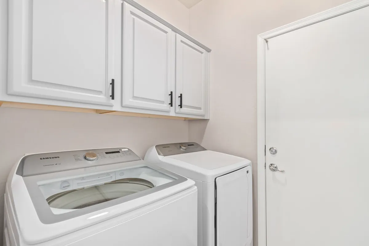 A functional and well-organized laundry room featuring a washing machine, dryer, and ample cabinetry for storage. The space is designed for efficiency and comfort, supporting extended stays and daily chores.