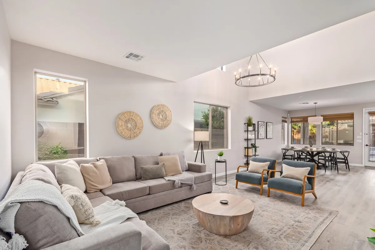 This image features a cozy living area arranged with a plush sofa, a central coffee table, an elegant chandelier overhead, and an adjacent dining table. Decorative wall hangings and soft lighting create an inviting atmosphere ideal for relaxation or entertaining. The scene is set for family gatherings or casual evenings with friends, underscoring the concept of a social, welcoming hub.