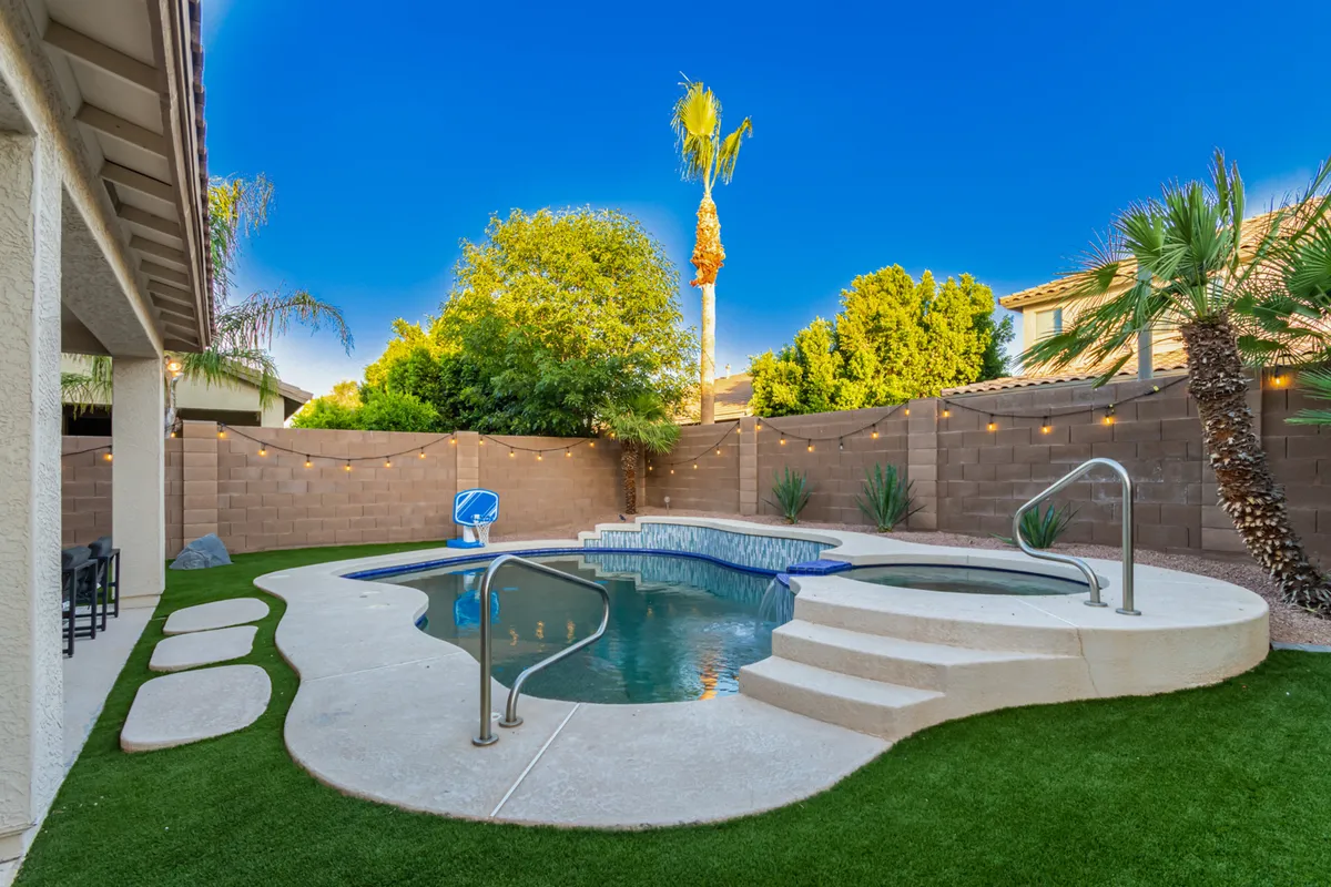 A beautifully landscaped backyard featuring a sparkling swimming pool and an adjacent jacuzzi (spa), set within a lush garden. Comfortable outdoor seating beckons for relaxation, and the overall setting is private and tranquil, ideal for both social gatherings and peaceful solitude.