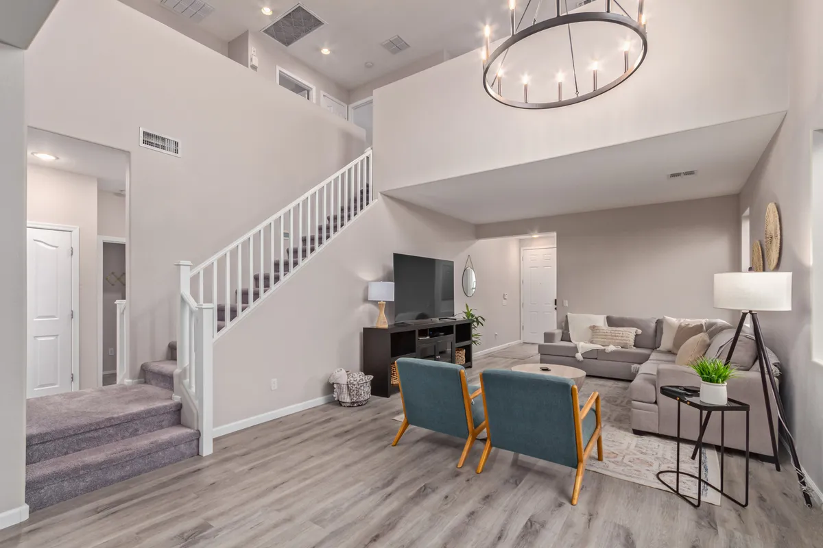 A comfortable, spacious living area features a large sofa and armchairs arranged for conversation or movie nights. The TV and chandelier add a touch of elegance, while the staircase hints at the upstairs loft, aligning with the section's reference to group indoor activities.