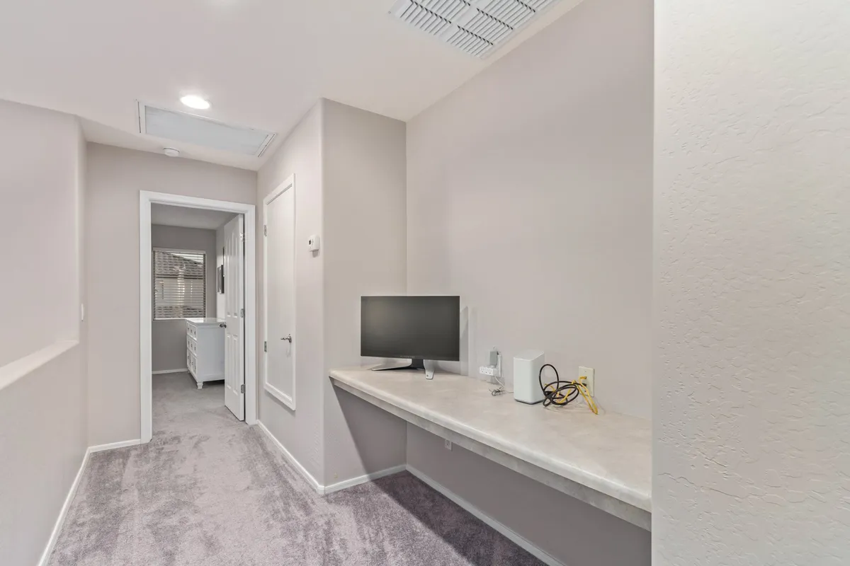A contemporary workspace set up with a desk and computer monitor, neutral-colored walls, and carpeted flooring. The area is organized and ready for productivity, reflecting thoughtful design for work-friendly stays.